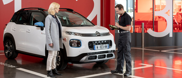 Senhora a ser atendida por técnico Citroen, na realização de uma extensão de garantia, Citroen C3 Aircross no fundo 